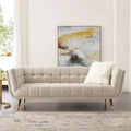Light beige tufted love seat or small sofa in a bright living room setting, accented with a white faux fur throw pillow, a gold lamp, and abstract art.