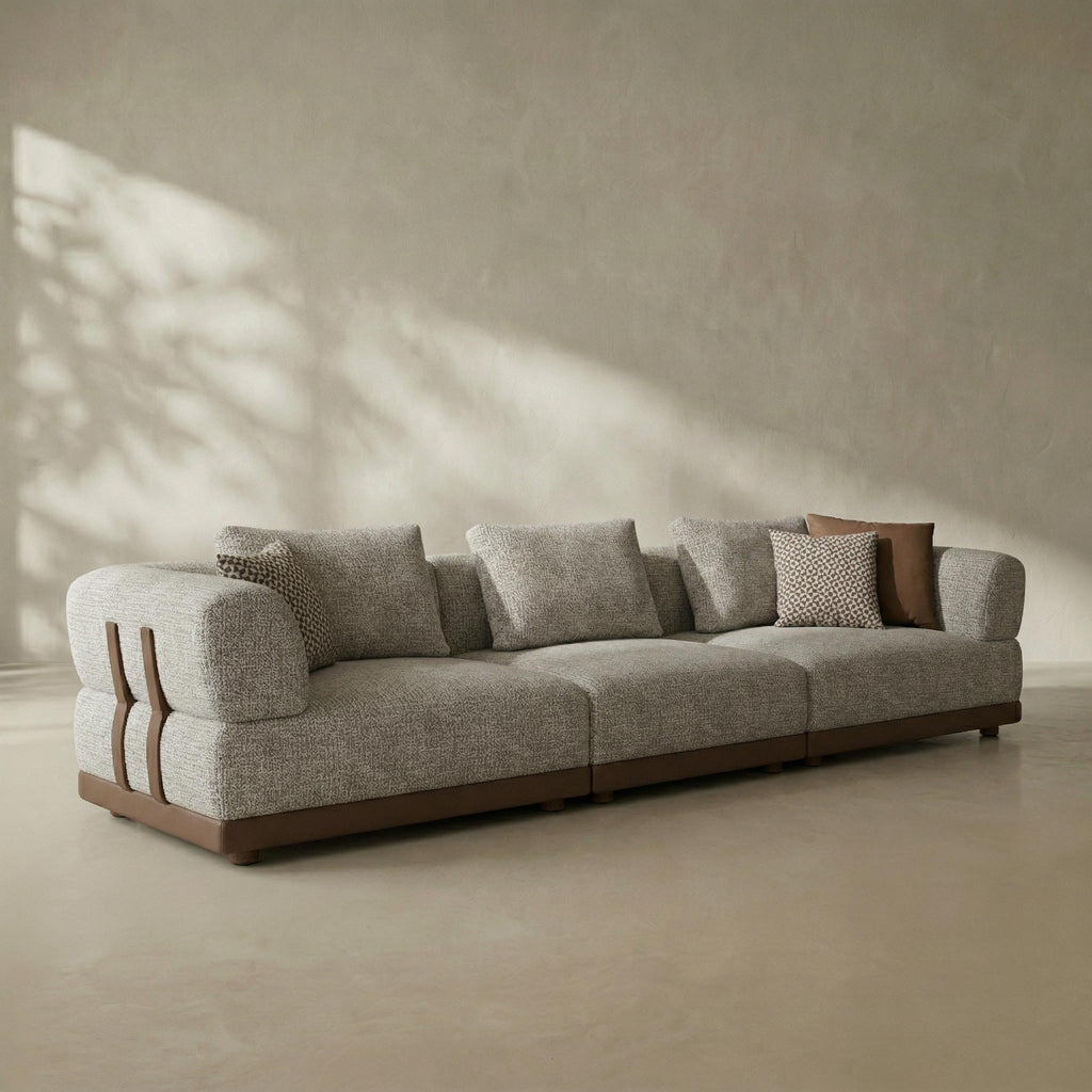 Gray sofa with wooden armrests in a minimalistic room with sunlight casting shadows on the wall.
