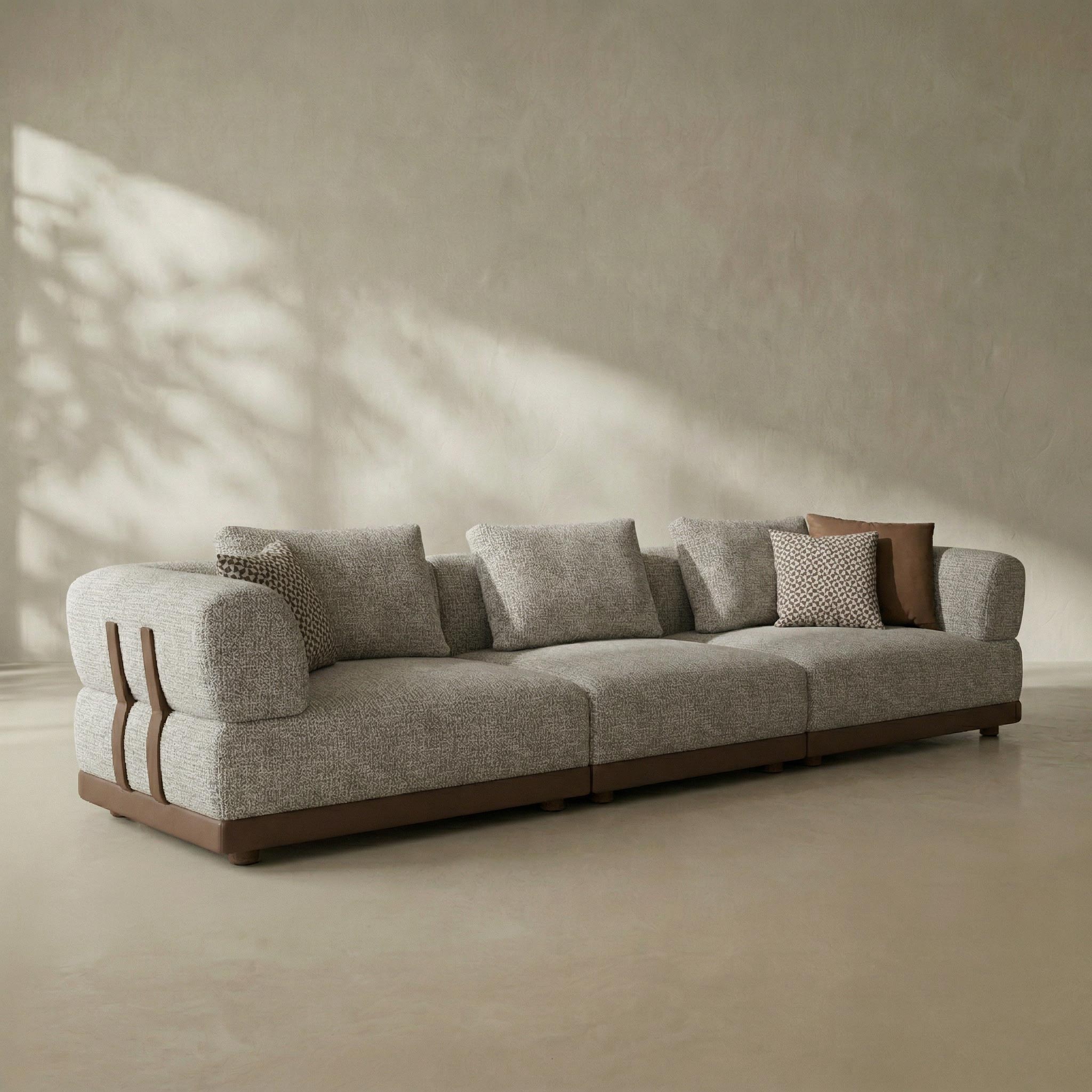 Gray sofa with wooden armrests in a minimalistic room with sunlight casting shadows on the wall.