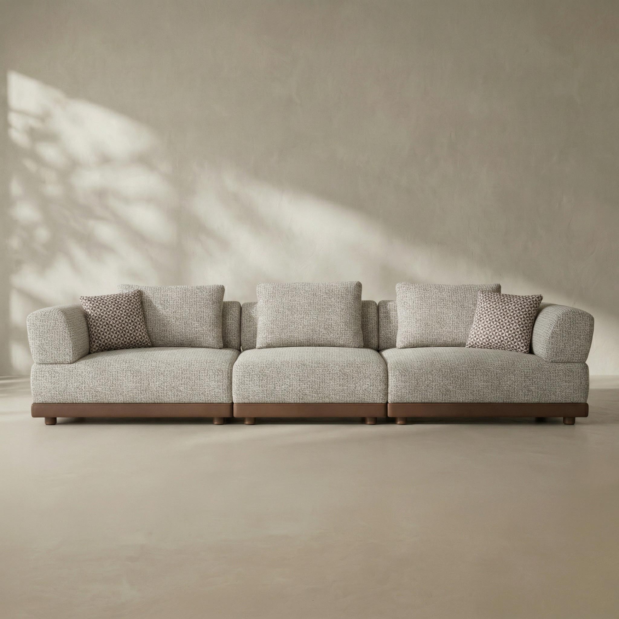 Gray sectional sofa with patterned cushions against a beige wall.