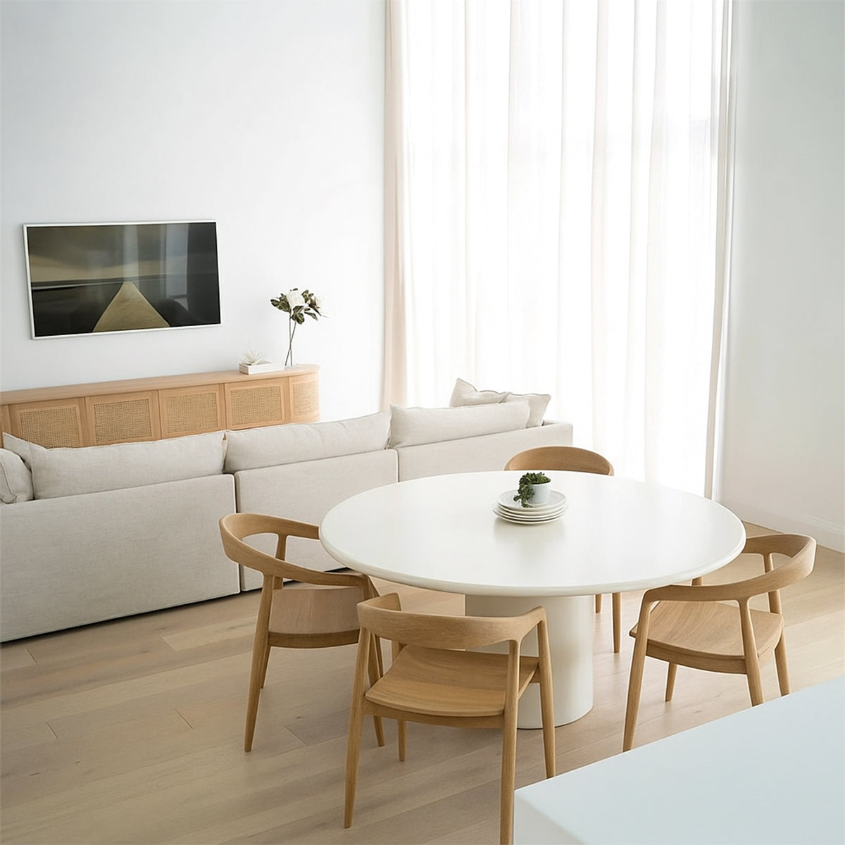 Dining area with a white round table and four wooden chairs set up.