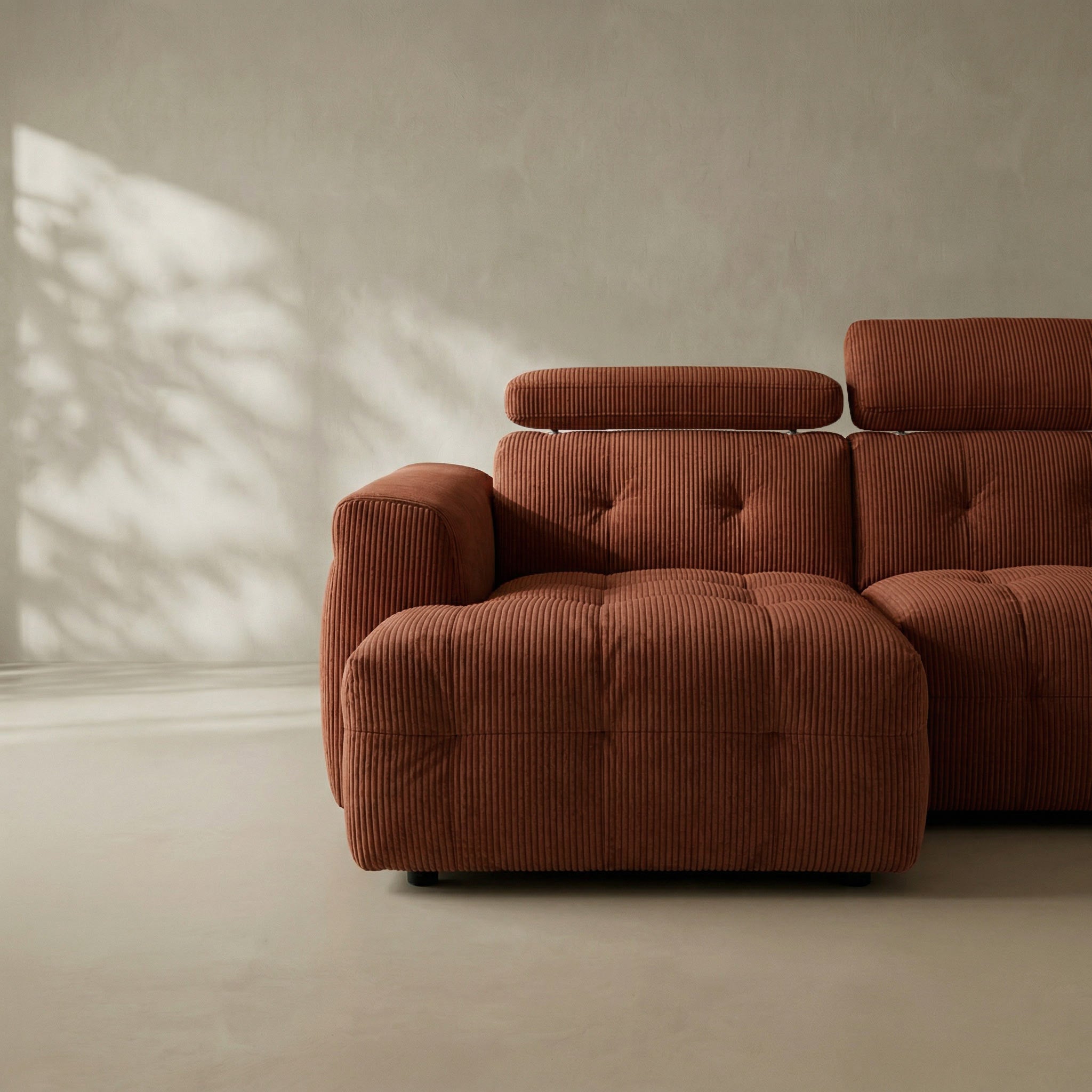 Brown corduroy sectional sofa in a minimalistic room with sunlight casting shadows.