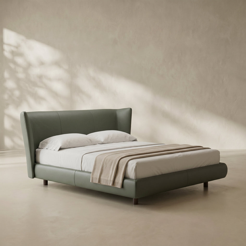 A modern upholstered bed with a tall curved headboard and matching footboard in muted sage green, styled with white bedding and a beige throw blanket in a minimalist room with warm natural light and leaf shadows.