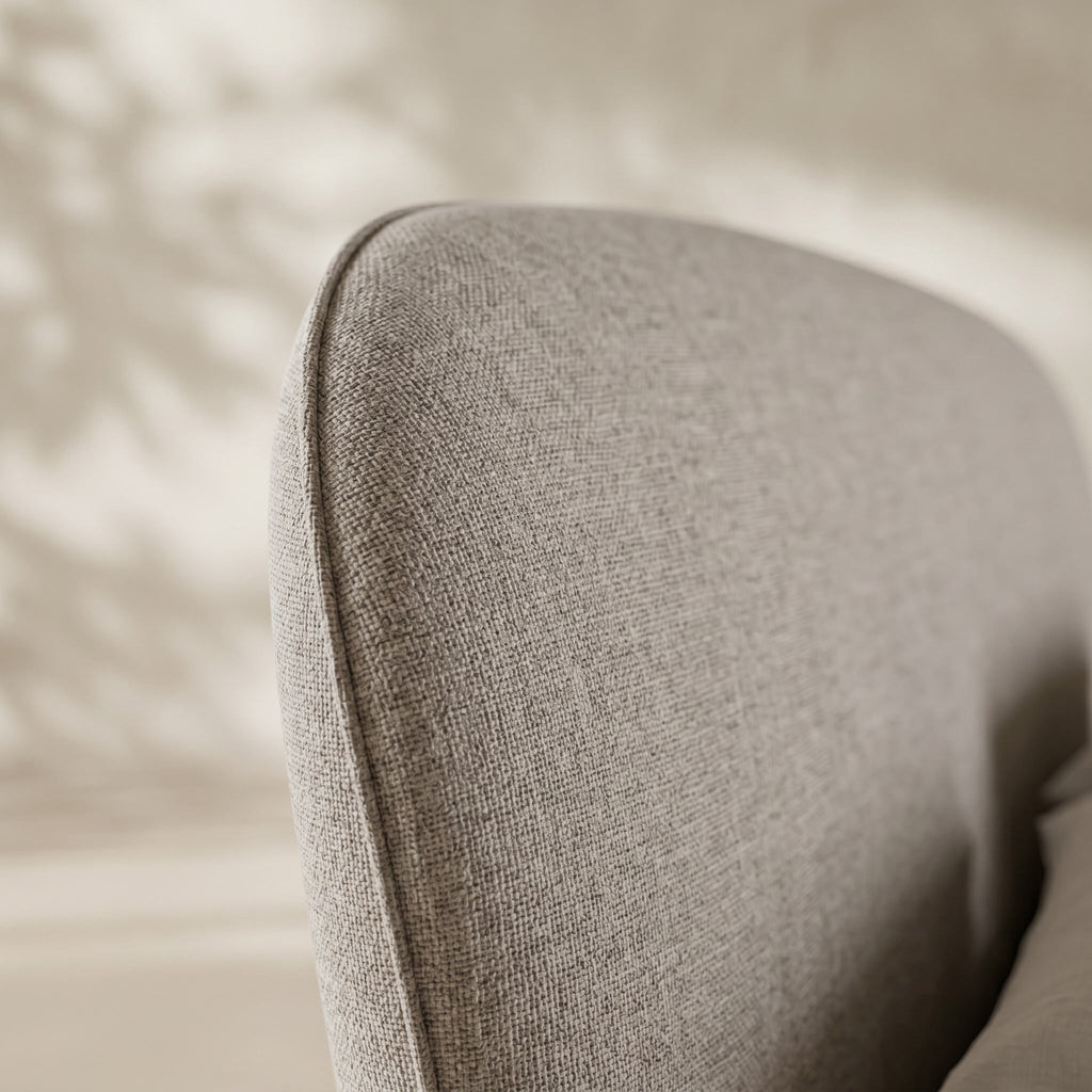 Close-up of a light gray textured fabric upholstered chair or cushion corner with soft warm shadows on a neutral beige background.