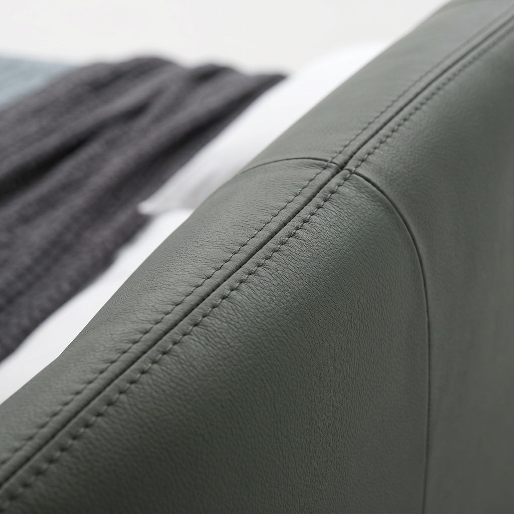 Close-up of a dark gray upholstered arm or cushion with visible stitching, shown against a softly blurred background with a dark knit textile and white surface.