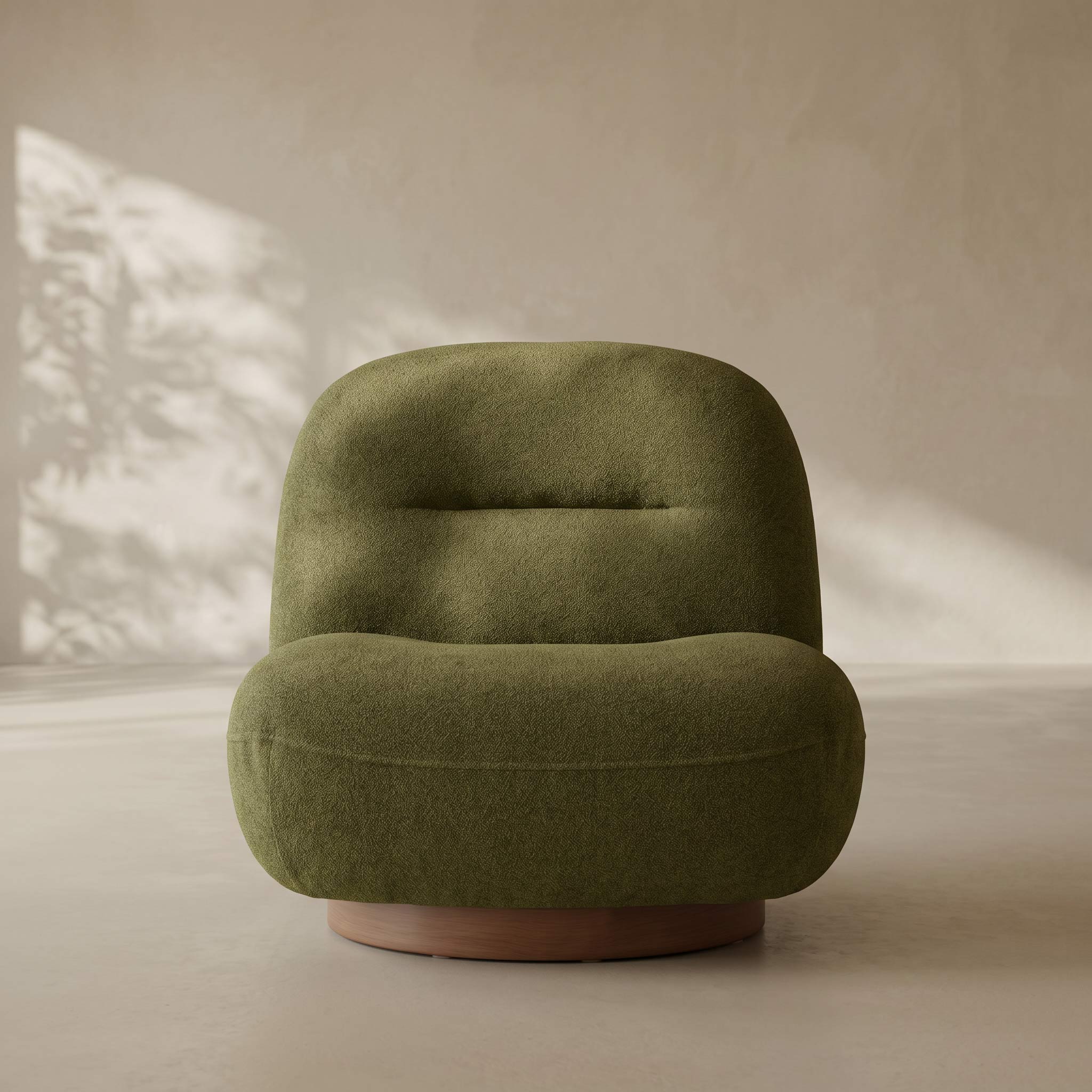 A modern, low-profile swivel armchair upholstered in textured olive green fabric, featuring a rounded backrest and a circular wooden base, set against a warm beige wall with soft leaf shadows.