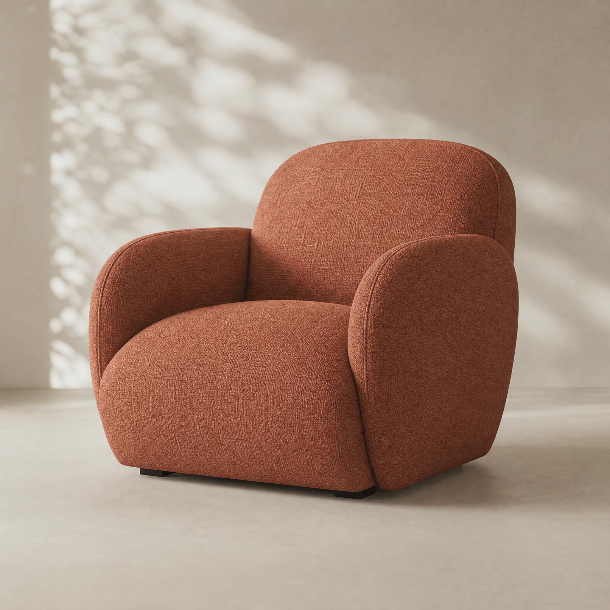 A modern low-profile armchair upholstered in textured terracotta orange fabric, set against a minimalist beige wall with soft leaf shadows.