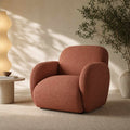 A modern armchair with rounded arms and a textured terracotta fabric, styled in a minimalist room with a wavy floor lamp, a small side table, and a potted plant.