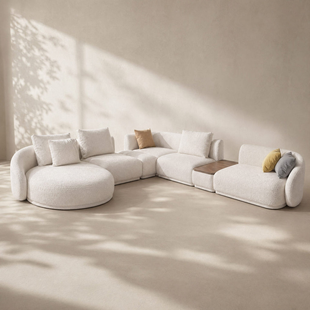 Modern white sectional sofa with cushions in a minimalistic room with sunlight filtering through.