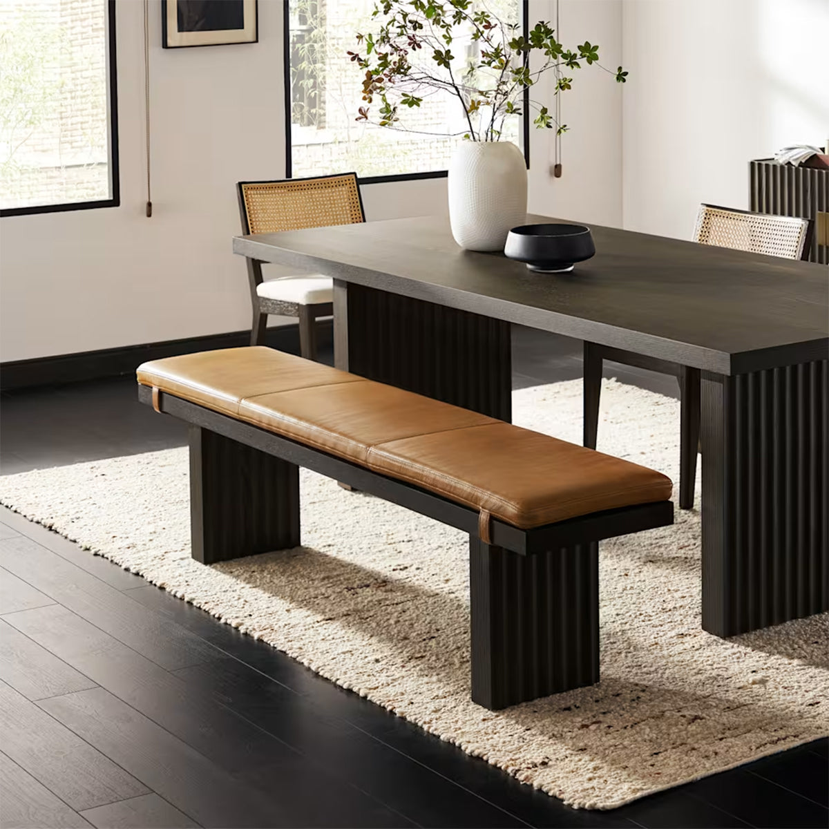Close-up showing the detail of the fluted dark wood table base and the cognac leather bench.