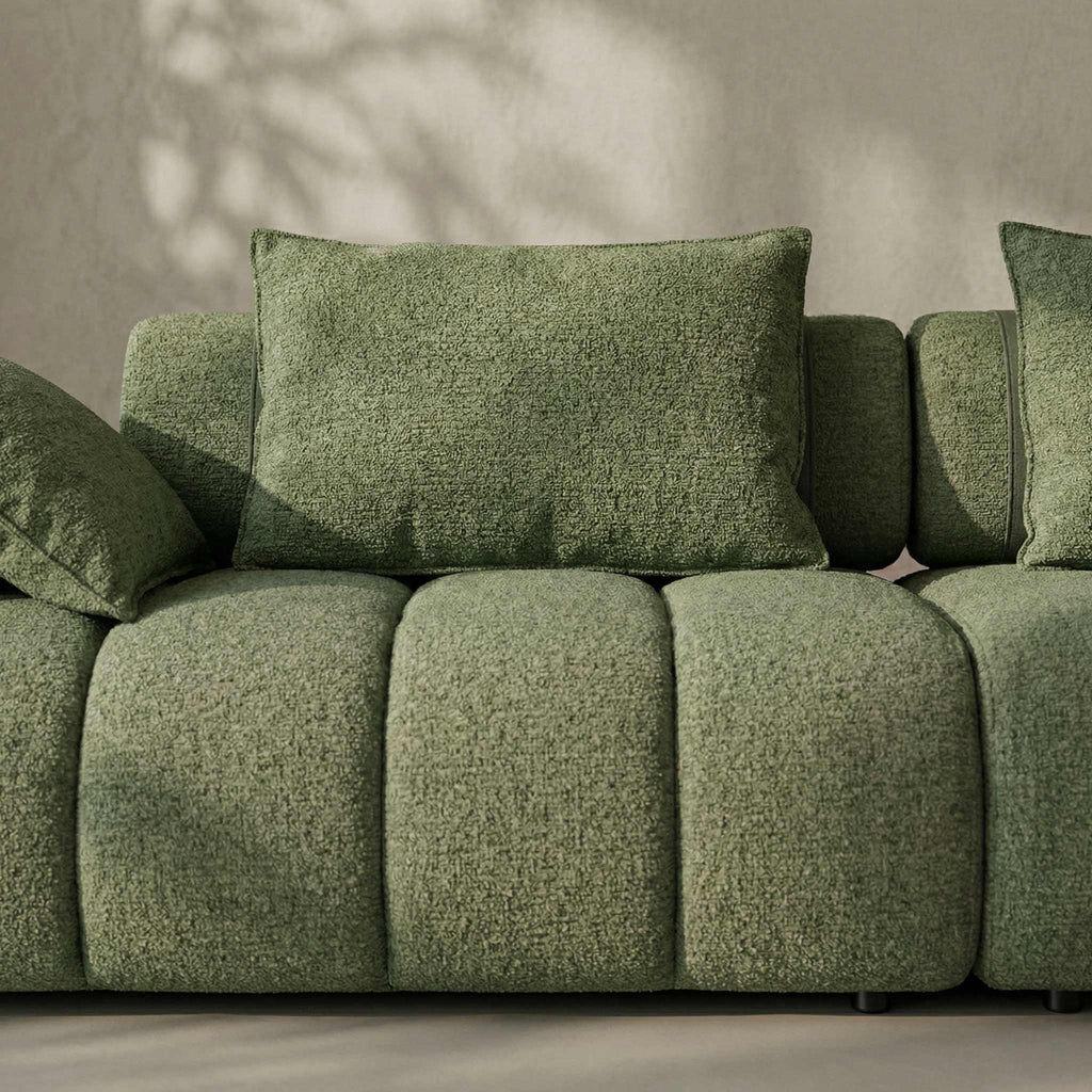 Green textured sofa with cushions against a neutral wall