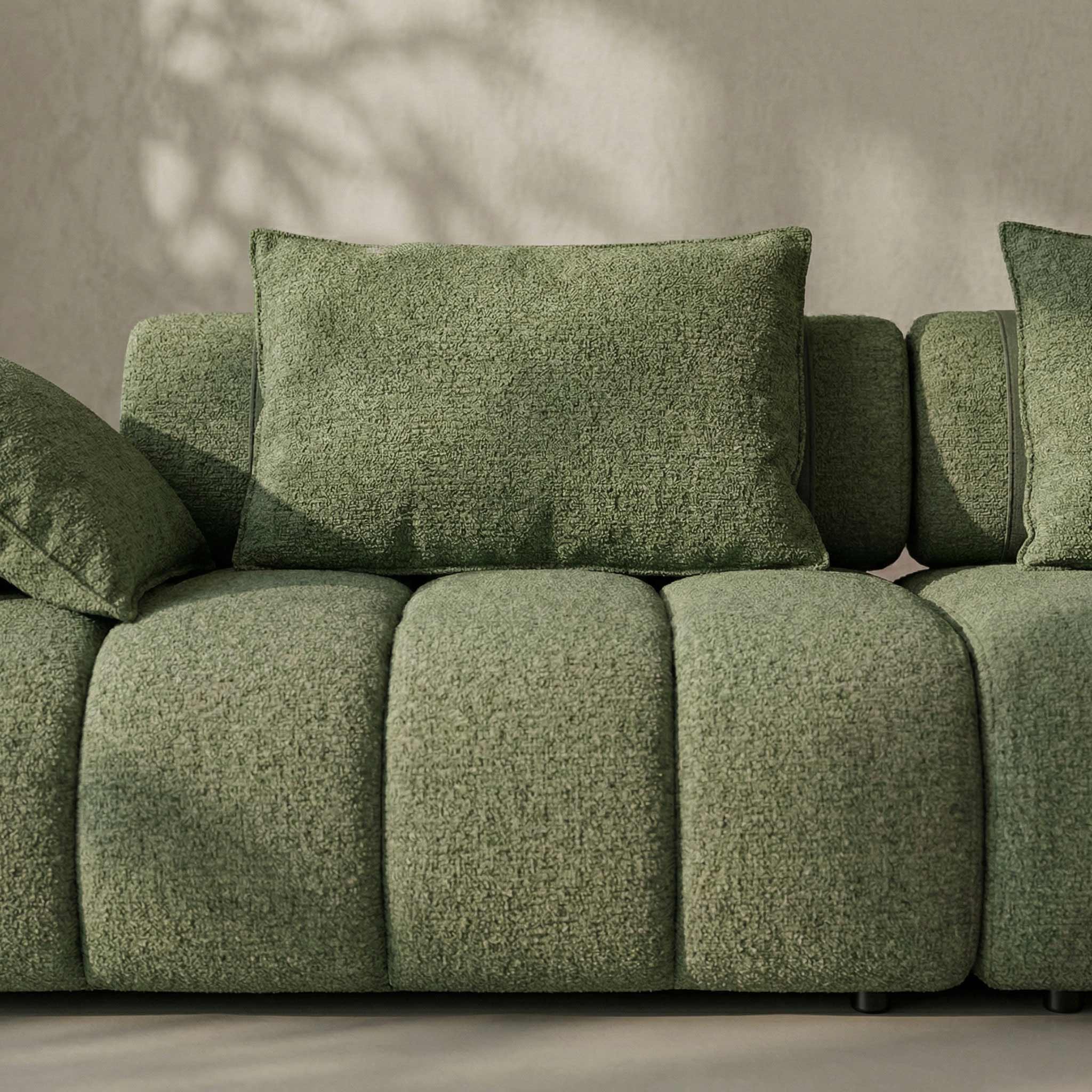 Green textured sofa with cushions against a neutral wall