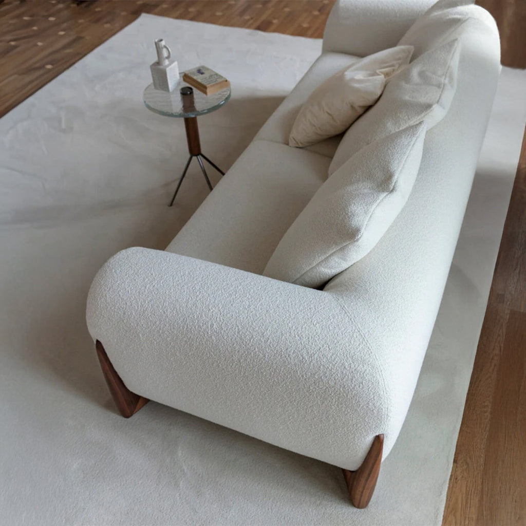 An elevated view of the back and armrest of a white sofa, showing the smooth, rounded lines and a small side table with a glass top.