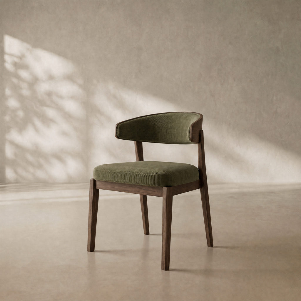 A modern accent chair with an olive green velvet upholstered seat and curved backrest, supported by a dark brown wooden frame, set against a textured beige wall with soft leaf shadows.
