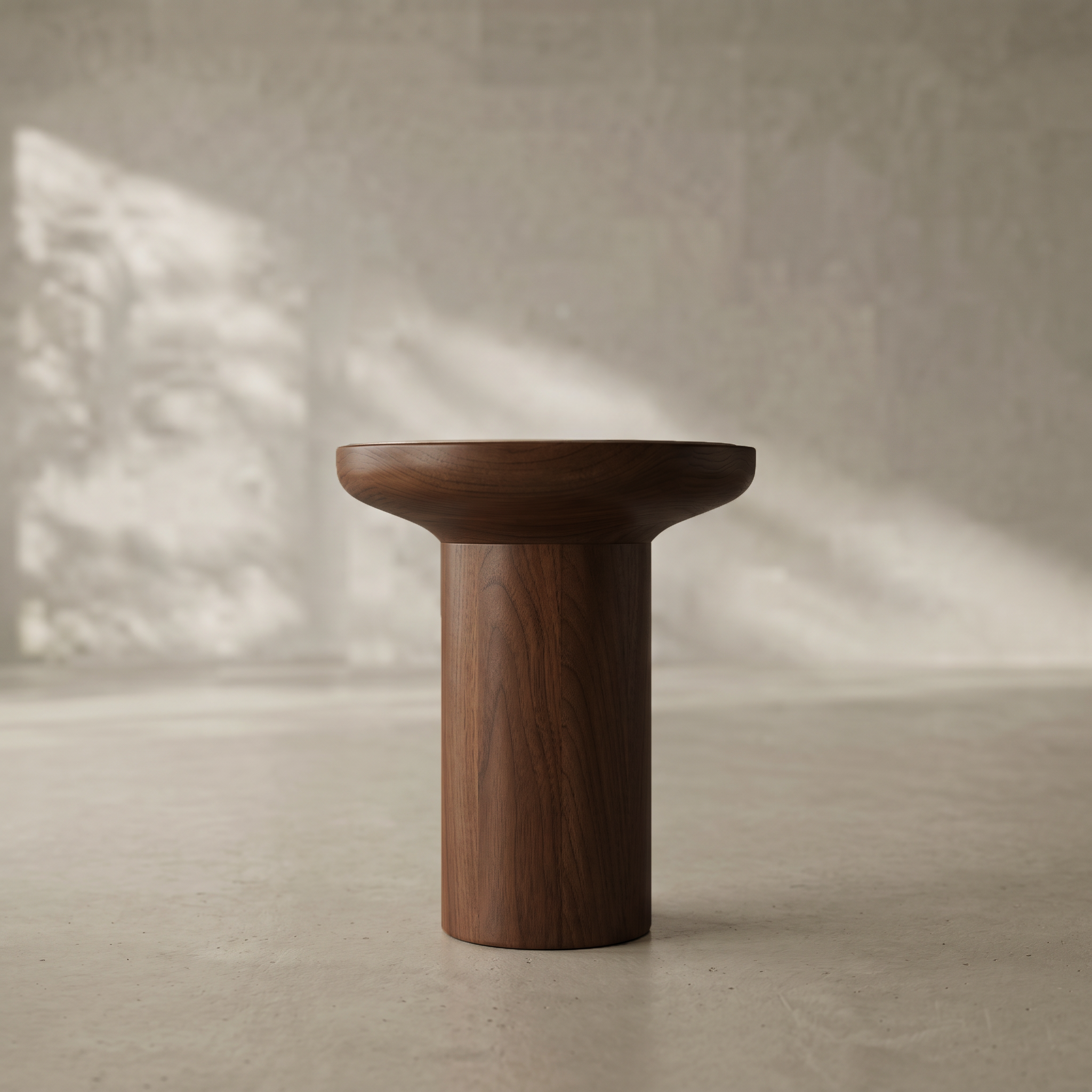 A dark brown wooden pedestal stool with a wide, rounded seat and a cylindrical base, set against a textured concrete wall and floor with soft natural light shadows.