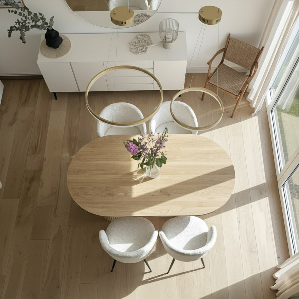 Overhead view of an oval wood dining table with four white boucle chairs in a bright modern room.