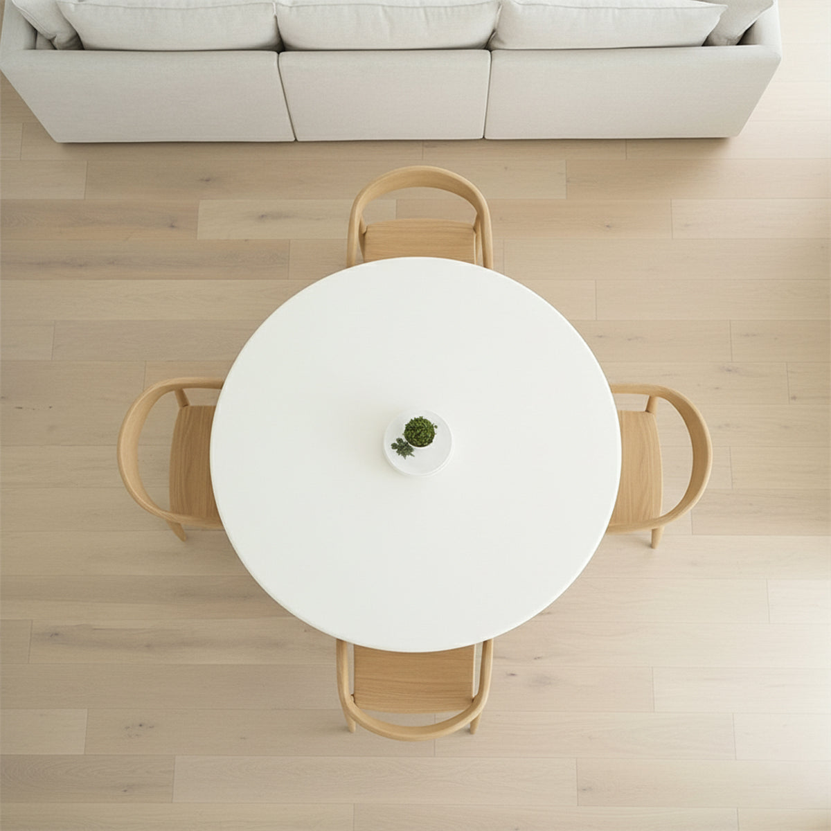 Top-down view of a white round dining table with four wooden chairs and a sofa in the background.