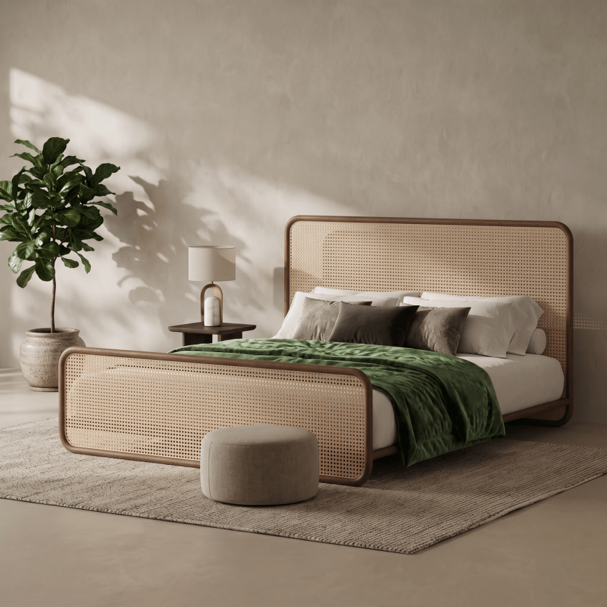 A modern bed with a woven cane headboard and footboard, styled in a minimalist bedroom with a green throw blanket, neutral pillows, a small side table with a lamp, a potted plant, and a round ottoman.