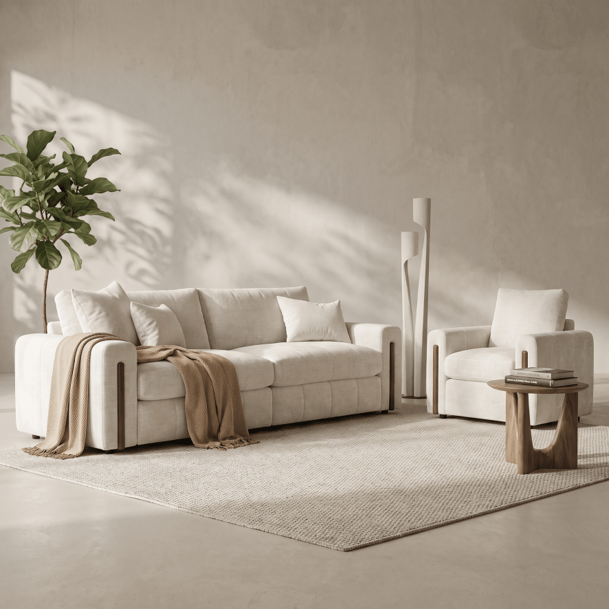 A modern living room setup featuring a cream-colored sofa and matching armchair on a textured light rug, with a small wooden side table, a tall potted plant, and a minimalist floor lamp against a textured beige wall.