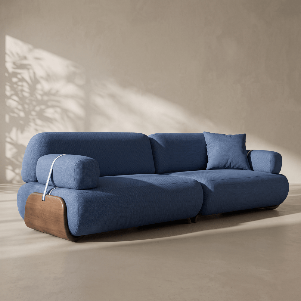 A modern blue upholstered sofa with rounded blocky cushions and a curved wooden base, shown in a minimalist interior setting with warm sunlight and shadow patterns on a textured beige wall.