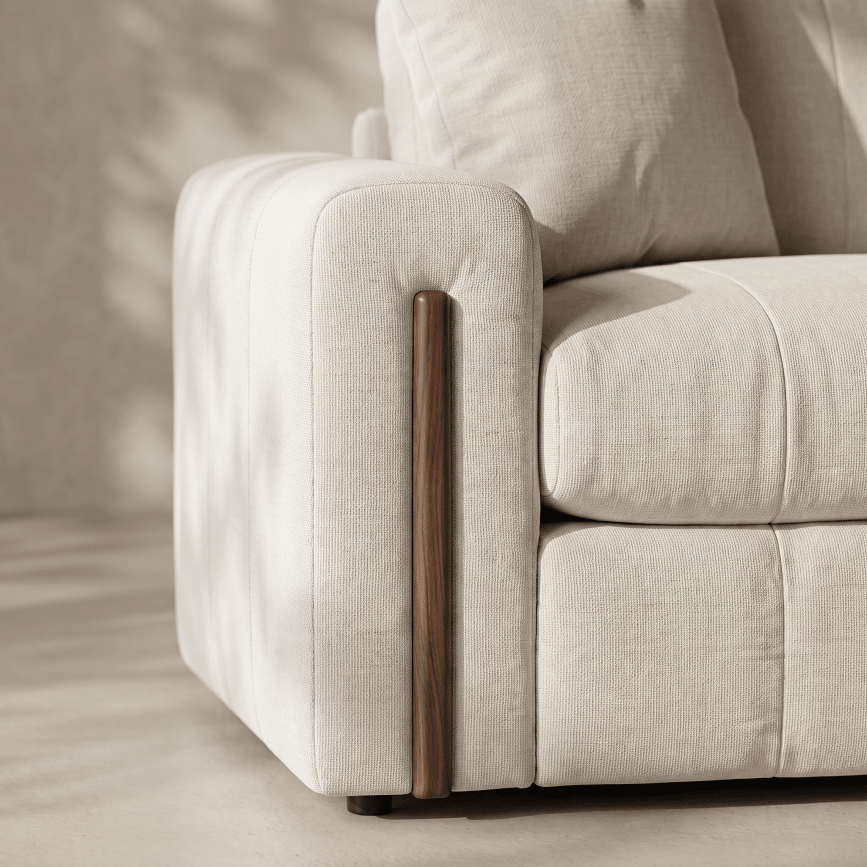 Close-up of a light beige upholstered sofa corner with a vertical dark wood accent panel on the armrest, set against a softly lit neutral interior background.