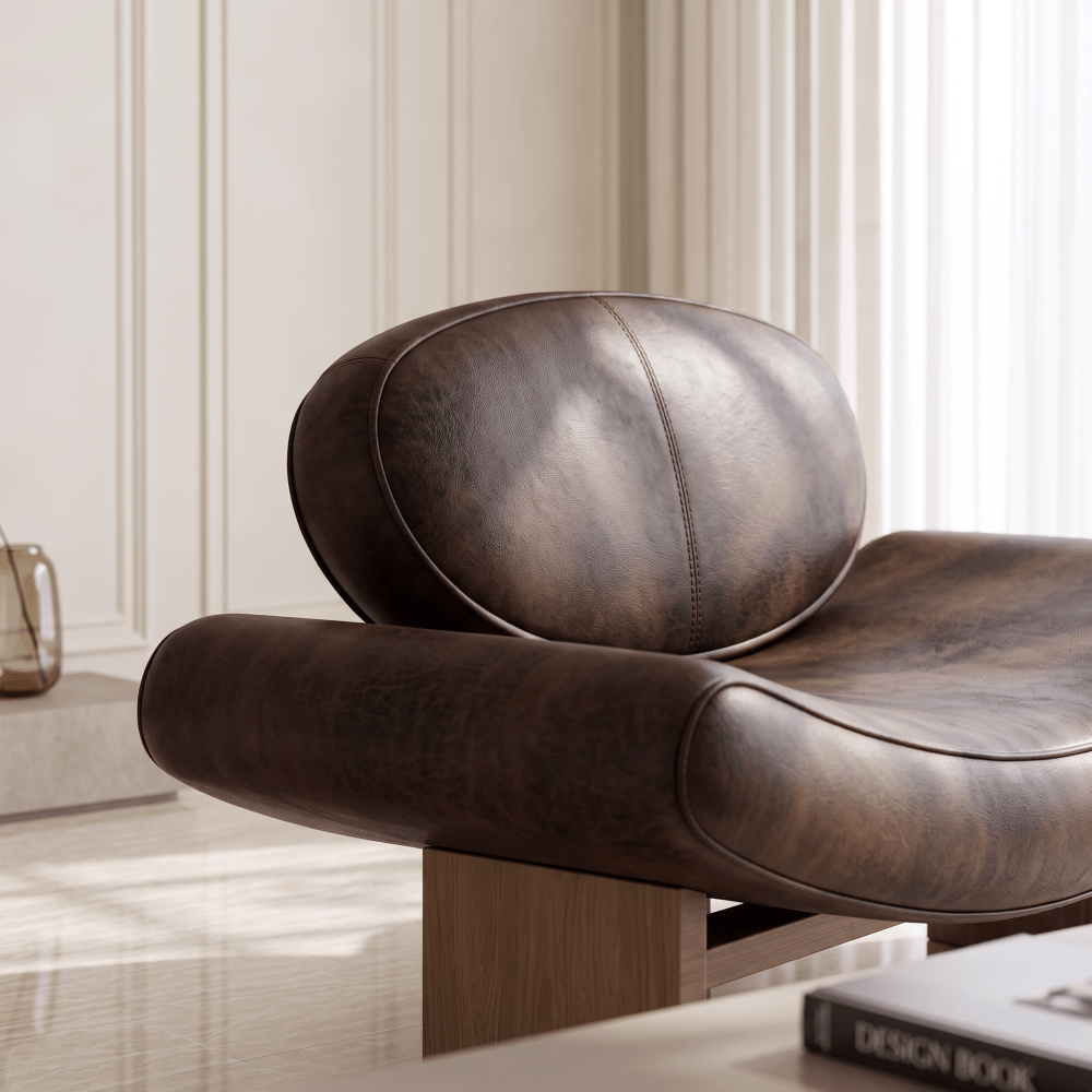 A close-up of a dark brown distressed leather lounge chair with a rounded backrest and wooden legs, set in a bright, modern room with cream paneled walls.