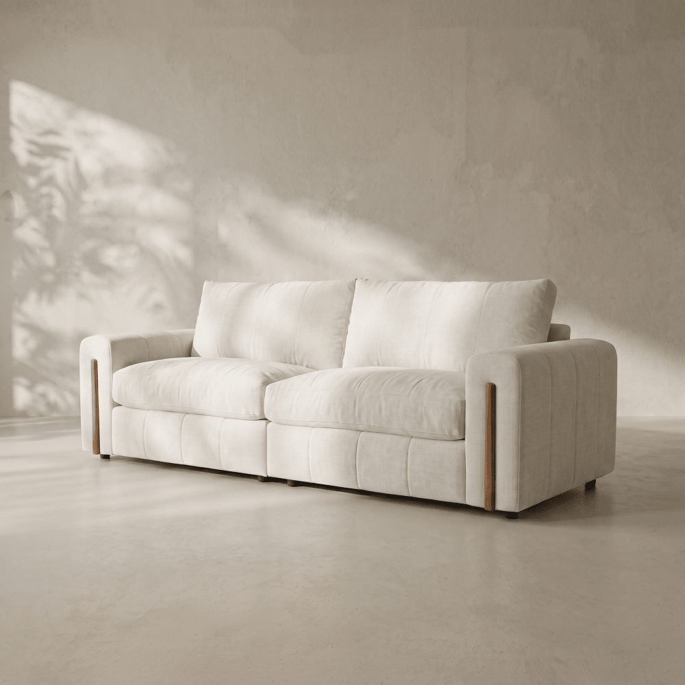 A modern two-seater sofa upholstered in a warm off-white fabric, set against a minimalist concrete wall with soft leaf shadows cast across it.