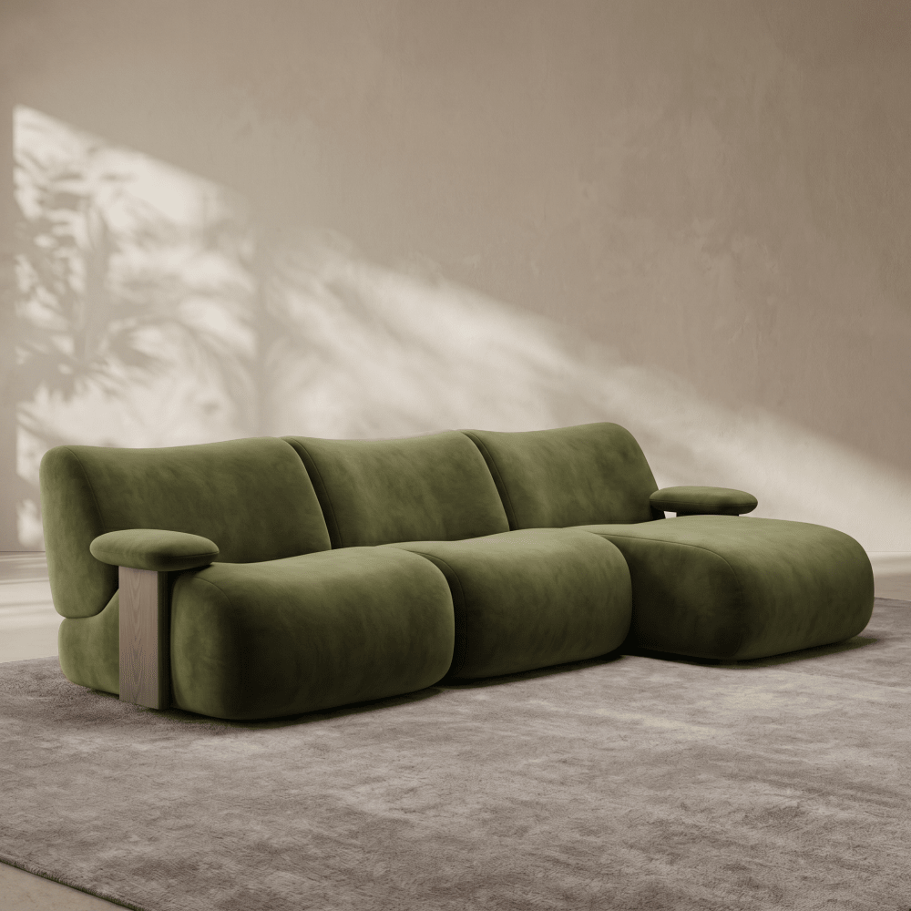 An olive green modular sectional sofa with a chunky, rounded design, set on a textured gray rug against a warm beige wall with soft leaf shadows.