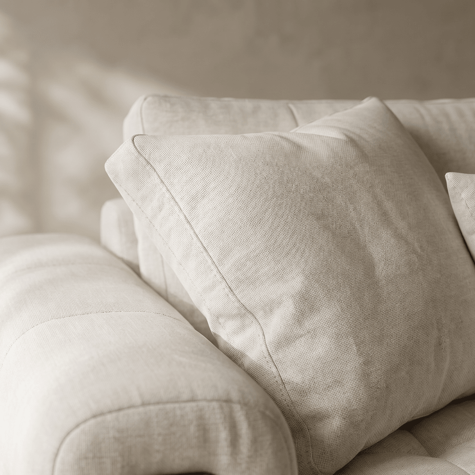 A close-up of a light beige textured throw pillow resting on a matching upholstered sofa in a softly lit interior.