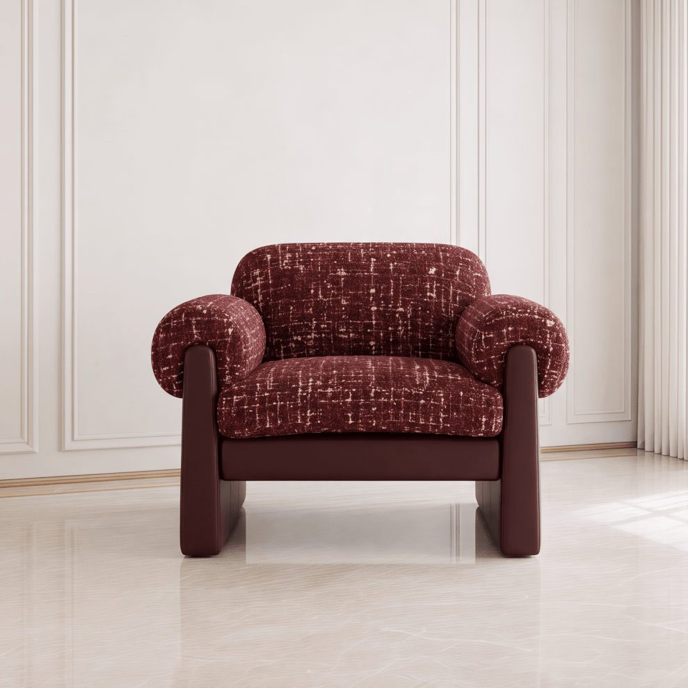 A single upholstered armchair with rounded arms and legs, shown centered in a bright interior. The chair has a textured burgundy fabric seat and back with dark brown leather-like arms and base.