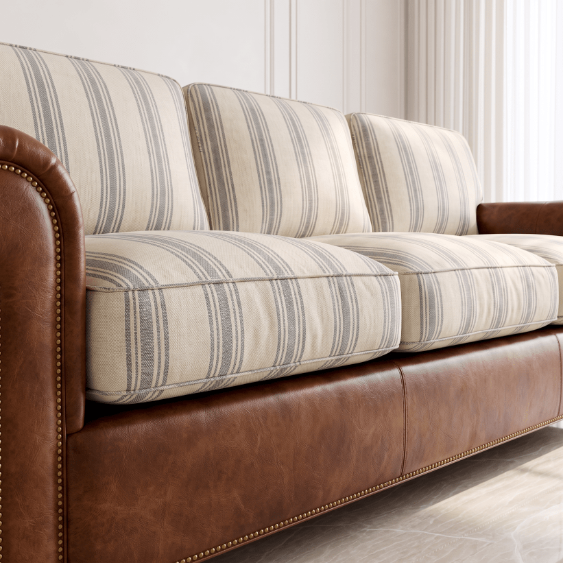 A close-up of a sofa with cream and gray striped upholstery on the seat and back cushions, paired with a brown leather base and armrests, shown in a bright interior setting.