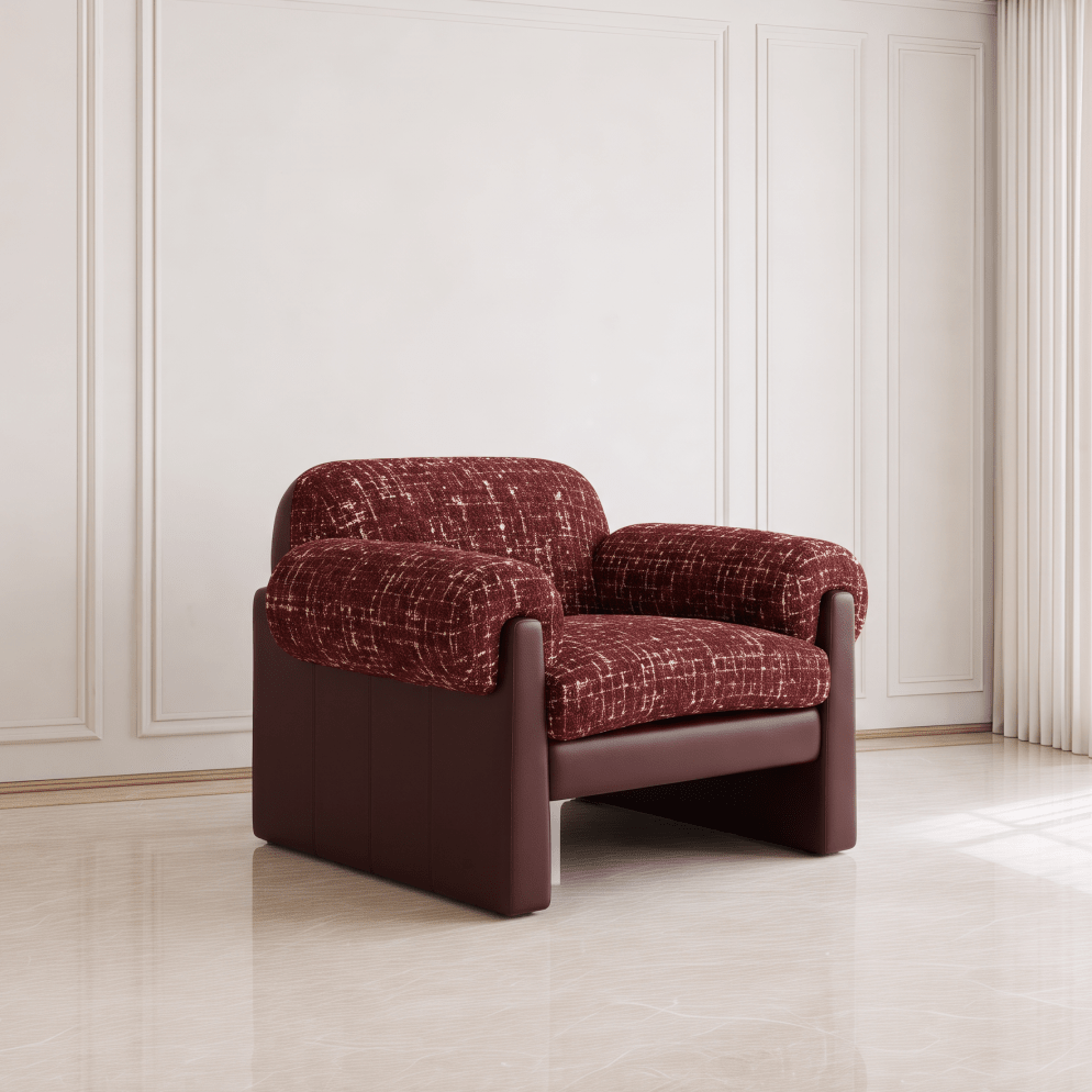 A modern armchair with textured burgundy bouclé upholstery and smooth dark brown leather-like sides and base, shown in a minimalist interior setting with cream paneled walls and light beige flooring.