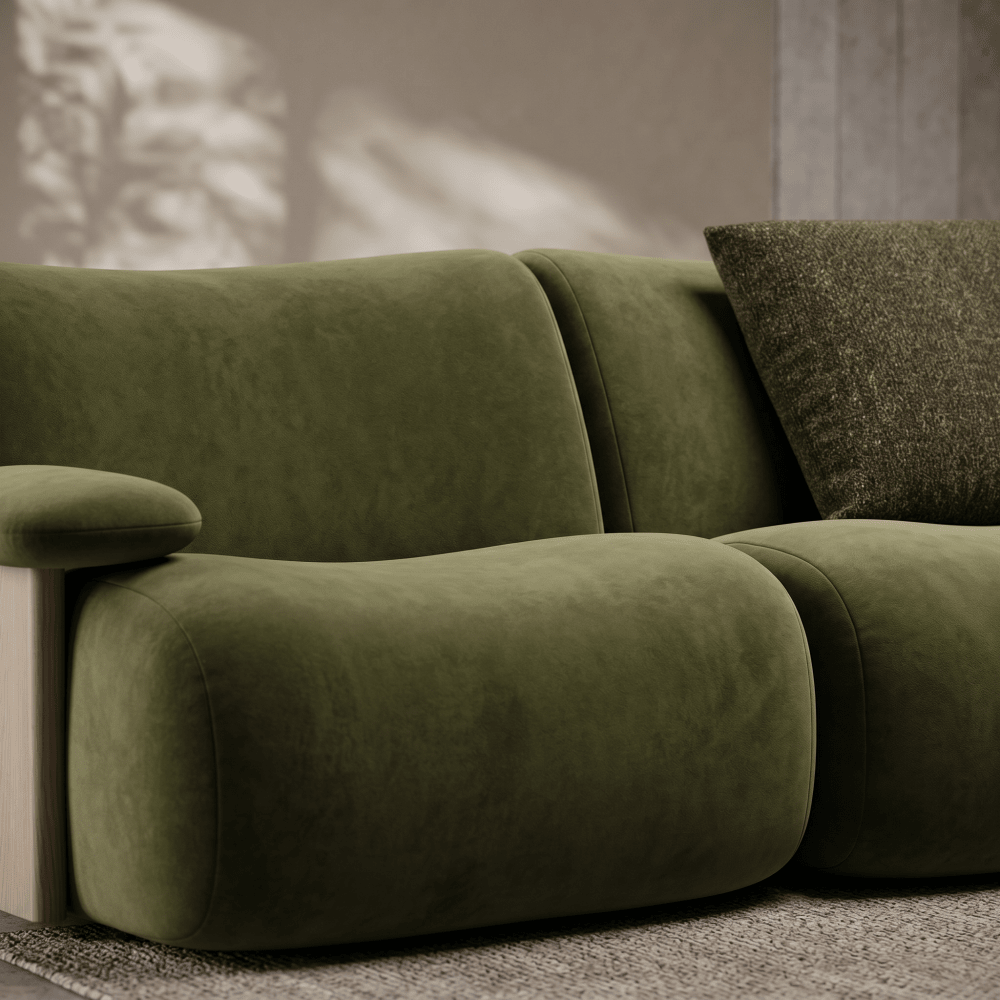 An olive green velvet modular sofa with a textured dark green throw pillow, shown in a modern living room setting with soft shadow patterns on the wall.