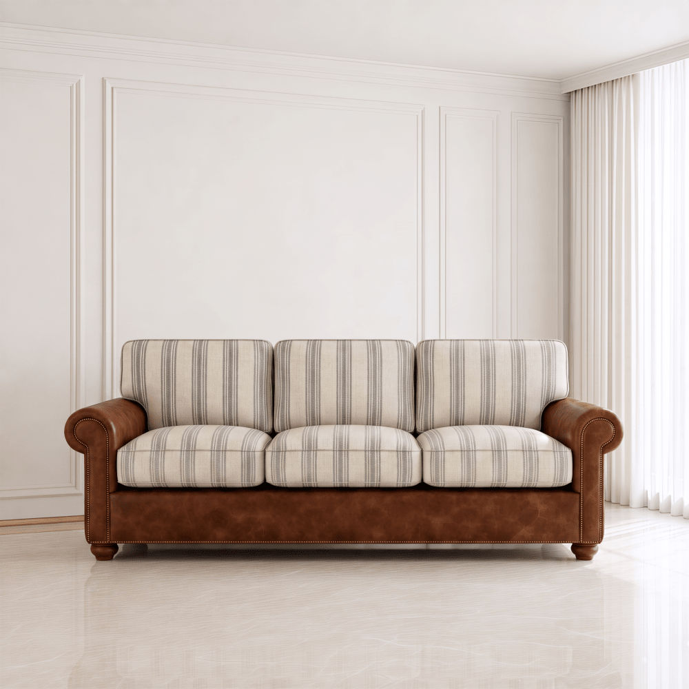 A three-seater sofa with cream and gray striped upholstery on the seat and back cushions, paired with a brown leather-look frame and rolled arms, set in a bright, modern room with white paneled walls and light-colored flooring.