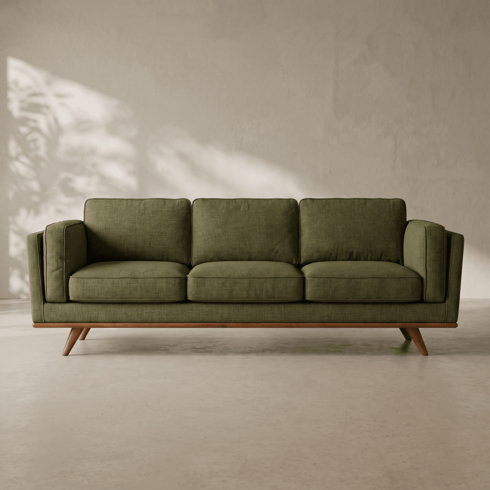 An olive green three-seater sofa with a mid-century wooden frame and tapered legs, set against a textured light gray wall with soft leaf shadows.