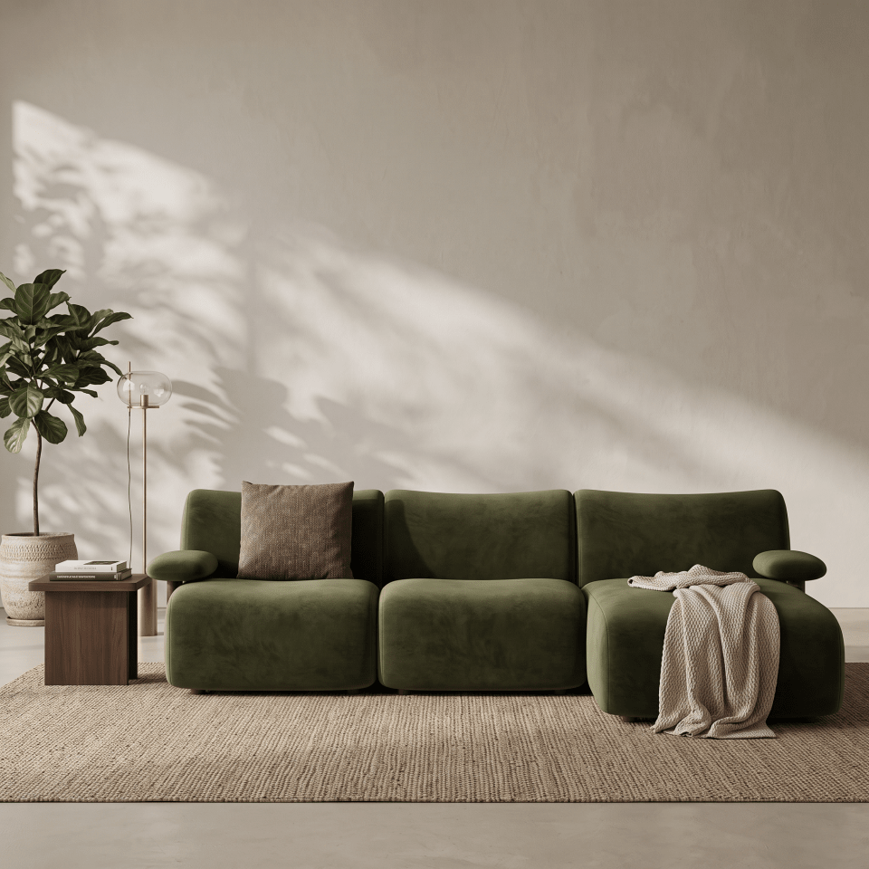 An olive green modular sectional sofa with a textured velvet-like finish, styled in a minimalist living room with a beige wall, a side table, a potted plant, and a draped throw blanket.
